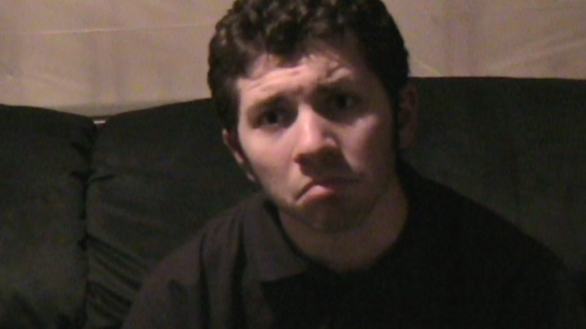 A screenshot from a video where Bryce Kalal is sitting on a couch, leaning forward, and pouting at something off-screen.