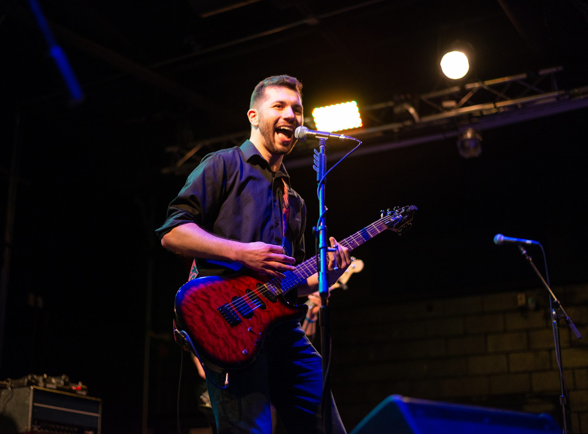 Bryce Kalal singing and playing a red guitar on stage at The Garage. He's smiling as he looks out to the crowd.